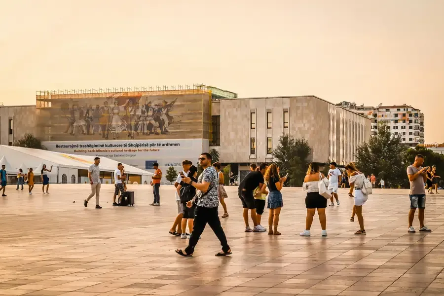 A public square in Tirana at sunset, with people crossing it